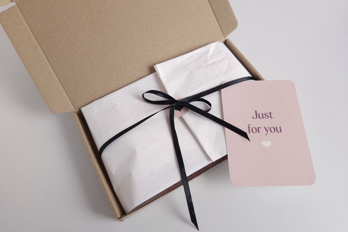 Ingepakte cadeaubox van CaDo Depot met wit vloeipapier, zwart lint en een kaartje met 'Just for you'.