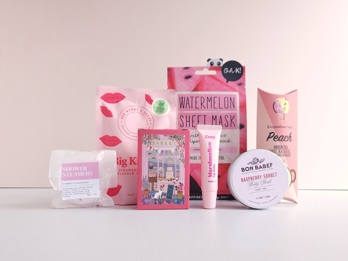 Producten uit een CaDo Depot cadeaubox: shower steamers, chocolade, sheet mask, lipbalm, body scrub en thee.